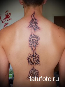 Фото тату с иероглифами, расположенными вертикально по позвоночнику. Четыре символа, выполненные в черном цвете, создают стильный и значимый рисунок татуировки.