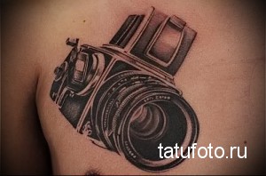 Фото тату на груди с изображением старинного пленочного фотоаппарата. Черно-белое исполнение, реалистичная детализация и тени.