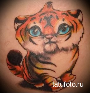 Фото тату милого тигренка на руке. Детализированный рисунок с яркими оранжевыми и черными полосками и большими голубыми глазами.