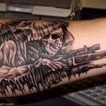 Фото тату на руке с изображением снайпера в маскировке, целившегося из винтовки, выполненное в реалистичном стиле.