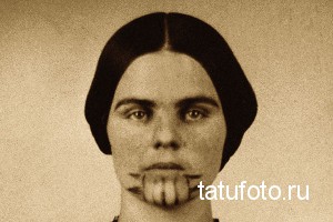 Старинное фото женщины с необычной татуировкой, изображающей зубы на ее нижней губе. Фотография выполнена в сепии.