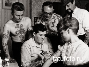 Фотография старой тату-студии, где мастер делает татуировку клиенту, окруженный другими людьми.