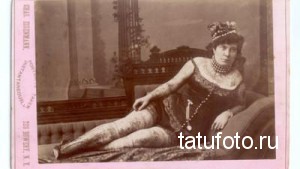 Старинная фотография женщины с татуировками на руках и ногах, одетой в элегантное платье.