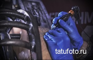 Фото процесса татуировки: мастер в синих перчатках наносит рисунок на кожу клиента. Видна тату-машинка и рука мастера.