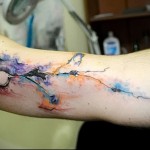Фото акварельной татуировки на руке. Яркий и красочный рисунок татуировки с размытыми красками и абстрактными формами.