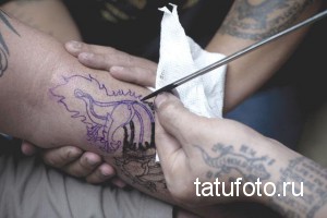 Фото процесса нанесения эскиза татуировки волка на руку. Мастер переносит рисунок на кожу.