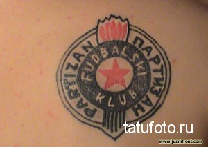 Фото тату на плече с изображением эмблемы футбольного клуба 'Партизан'. Эмблема выполнена в черно-красных тонах и имеет круглую форму.