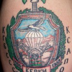 Фото татуировки с изображением щита, парашютиста и надписей 'КГБ', 'ССР', 'КСАП'. Изображение выполнено в черно-серых тонах.