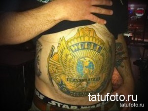 Фото татуировки на животе с изображением логотипа World Heavy Metal. Логотип выполнен в ярких цветах с использованием желтого, красного и синего.