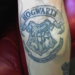 Фото тату: изображение герба Хогвартса из серии книг и фильмов о Гарри Поттере. Детализированный рисунок, выполненный в серо-синих тонах.