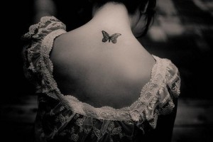 Фото тату маленькой бабочки на спине девушки. Черно-белый рисунок с тонкой прорисовкой и нежным дизайном.