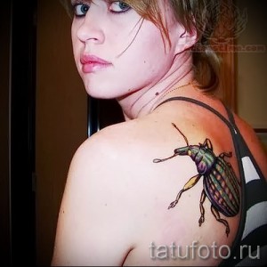Фото татуировки с изображением красочного жука на плече девушки. Реалистичный стиль и яркая цветовая палитра.