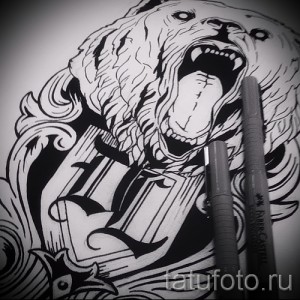 Фотография черно-белой татуировки медвежьей головы с открытой пастью и клыками, украшенной стилизованным леттерингом.