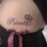Фото татуировки с надписью 'Princess' и изображением короны на талии. Черно-серый рисунок татуировки, выполненный каллиграфическим шрифтом.