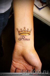 Фото тату на запястье: золотая корона с драгоценными камнями и надпись 'Prince'. Элегантный рисунок татуировки в реалистичном стиле.