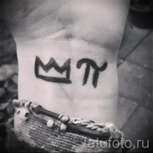 Фото тату на запястье: простая черная корона и буквы 'M' и 'П'. Минималистичный рисунок татуировки в графичном стиле.