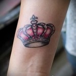 Фото тату на запястье: розовая корона с серебряными контурами и драгоценными камнями. Элегантный рисунок татуировки в нежном стиле.