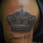 Фото тату на плече: большая корона с крестом наверху и надписью 'James 1:12'. Религиозный рисунок татуировки в черном цвете.