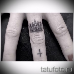Фото тату на пальце: крошечная корона с драгоценными камнями, выполненная в черном цвете. Нежный и изящный рисунок татуировки.