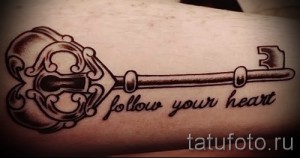 Фото татуировки в виде старинного ключа с надписью "Follow Your Heart". Черно-серый рисунок на руке.