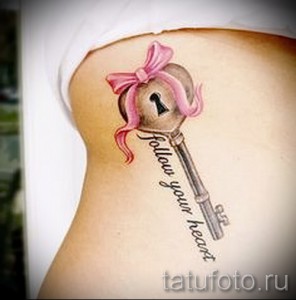 Фото тату на боку: ключ с розовым бантиком и надписью "Follow your heart". Цветная татуировка в нежном и романтичном стиле.