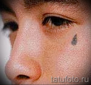 Фото тату слезы под глазом, выполненной в черном цвете. Рисунок выглядит как настоящая слеза, стекающая по щеке. Идея для тату, минимализм.
