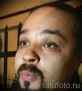 Фото тату маленькой слезы под глазом мужчины. Минималистичный рисунок татуировки, выполненный черным цветом, символизирующий печаль или потерю.