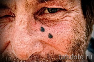 Фото мужчины с минималистичной татуировкой в виде двух точек на щеке. Сдержанный и необычный дизайн, привлекающий внимание.