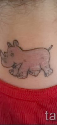Тату смешной носорог на шее сзади у девушки