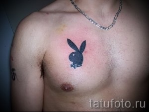 Фото татуировки с логотипом Playboy на груди. Черный рисунок, минималистичный стиль, культовый символ.