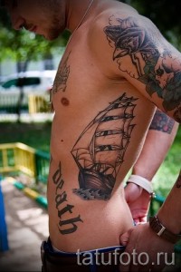 Фото тату парусника на боку. Черно-серый рисунок с детальной проработкой корабля и волн. Рядом с татуировкой надпись 'Death' готическим шрифтом.