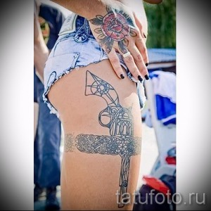 Фото тату на бедре: топор, выполненный в кельтском стиле с орнаментами, выполненный в черно-серых тонах. Мужественный рисунок татуировки с историческим значением.