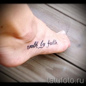 Фото тату: небольшая надпись 'walk by faith' черным цветом на внутренней стороне стопы. Изящный шрифт, минималистичный дизайн.