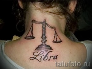 Фото тату Весы с надписью 'Libra' на шее, выполненная в черно-белых тонах. Детализированный рисунок с использованием различных оттенков серого.