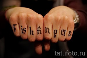 Фото тату надписи 'Fishfingers' на костяшках пальцев. Черно-белая татуировка, выполненная готическим шрифтом, вызывающий и провокационный дизайн.