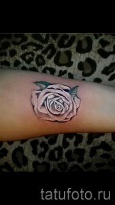 Фото тату: маленькая роза на запястье, стиль blackwork, четкие линии, минималистичный рисунок татуировки, женская рука.