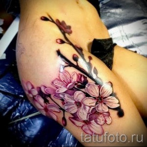 Фото тату: реалистичная ветка сакуры с розовыми цветами на руке. Детальная проработка лепестков и листьев, яркие цвета.