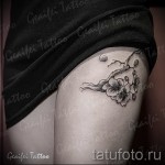 Фото тату: изящная черно-серая татуировка ветки сакуры с цветами и бутонами, расположенная на женской лопатке. Детализированный рисунок в стиле графика.