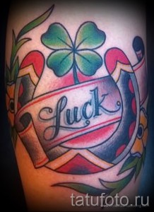 Фото тату с изображением подковы, четырехлистного клевера и ленты с надписью "Luck". Детализированный рисунок татуировки в ярких цветах.