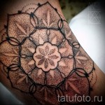 Фото тату: сложная мандала, выполненная точками (dotwork) на локте. Черно-серая татуировка с геометрическими узорами и тонкими линиями.