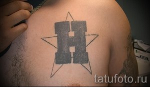 Фото тату буквы 'H' внутри звезды на груди, выполненной в черном цвете, минималистичный и лаконичный дизайн.