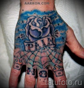 Фото тату: роза и надпись "PAIN IS NO SORROW" на ладони, синие и черные цвета, паутина, смелый дизайн.