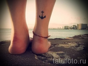 Фото татуировки с изображением черного якоря на лодыжке. Простой и лаконичный рисунок в морском стиле.