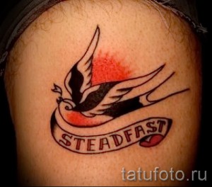 Фото тату ласточки с надписью Steadfast на руке. Черно-белая татуировка в стиле олд скул.