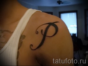 Фото тату буквы 'P' на плече. Черно-белая татуировка в каллиграфическом стиле.