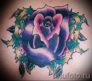 Фото тату: красочная роза с зелеными листьями и красными брызгами краски на коже. Идеальный эскиз тату для любителей ярких и необычных рисунков.