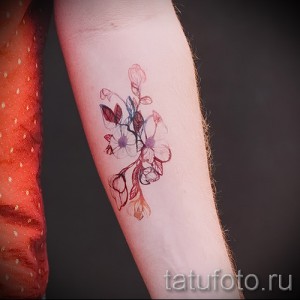Фото акварельной татуировки с изображением веточки цветущей сакуры. Легкие, размытые линии и пастельные тона создают эффект воздушности и нежности.