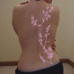 Фото тату: длинная ветка цветущей сакуры с розовыми цветами на спине девушки. Красивый рисунок татуировки.