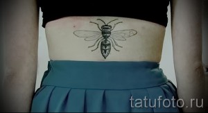 Фото тату: маленькая черная татуировка пчелы, расположенная на женском животе. Минималистичный дизайн с четкими линиями.