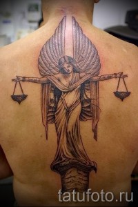 Фото тату Весы на спине, изображающее богиню правосудия с весами и крыльями. Детализированная татуировка в стиле реализм.